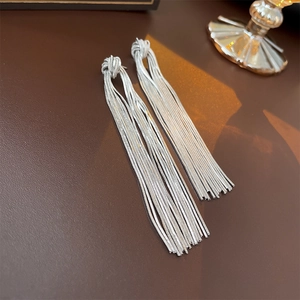 Detail shot of elegant silver knotted tassel earrings on premium leather texture