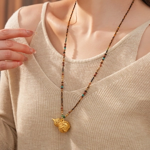Detailed view of a golden hollow gourd pendant on a colorful tiger eye beaded necklace