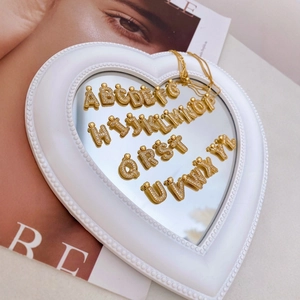 Luxury gold initial letter pendants with crystal inlay on a white heart shaped mirror