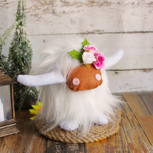 Close-up of white plush Highland cow with floral crown on rustic wooden base