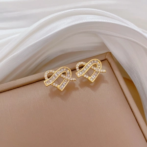 Macro shot of gold heart-shaped stud earrings with sparkling cubic zirconia on white silk
