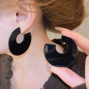 Macro detail of large black acrylic C-shaped earrings with glossy finish and silver pins