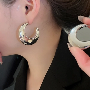 Close-up of model wearing large silver C-shaped metal hoop earrings with high gloss finish