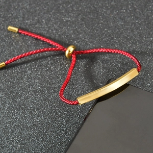 Close-up of red braided rope bracelet with polished gold-plated metal bar and adjustable slider