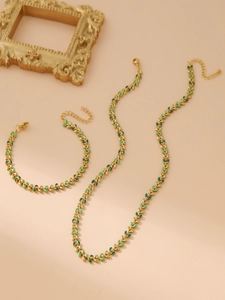 Detail of gold leaf necklace and bracelet set with green enamel on a pink background