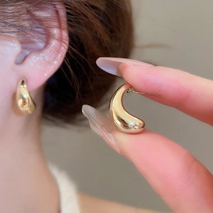 Detailed view of gold teardrop earrings with a polished mirror finish on model and in hand