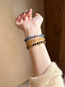 Detail of layered tiger eye and citrine beaded bracelets with gold coin charms