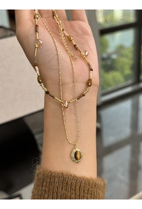Close-up of layered necklace with oval tiger eye pendant and gold-plated beaded chains