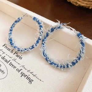 Detail of blue denim wrapped C-shaped hoop earrings with raw frayed edges on white stand