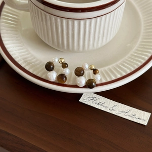 Close-up of geometric tiger eye and pearl hoop earrings on a vintage coffee saucer