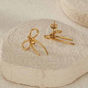 Detail view of gold stainless steel bow earrings on minimalist stone surface background