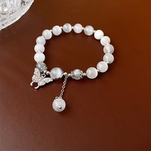 Gros plan d'un bracelet papillon avec perles en œil de chat et pompon argenté