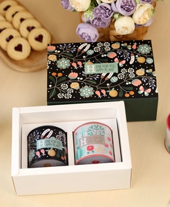 Deep green gift box set with two floral tin canisters on a warm beige table