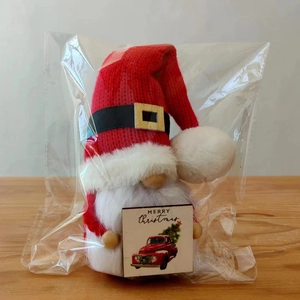 Macro view of Christmas gnome with red knit hat holding a Merry Christmas wooden card