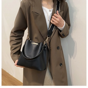 Detail of black PU leather bucket bag with wide patterned strap on model in brown blazer
