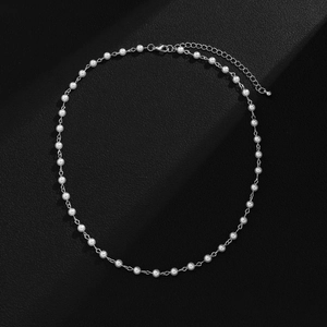 Detail einer minimalistischen Perlenkette mit Metallgliedern und Karabiner auf schwarzem Leder