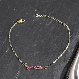 Detail of gold Arabic love charm bracelet with micro-paved ruby zircons on slate