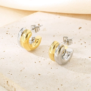 Gros plan de boucles d'oreilles créoles C bicolores or et argent sur pierre mate