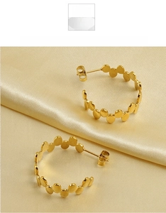 Detailed view of C-shaped gold hoop earrings with layered discs on gold silk fabric