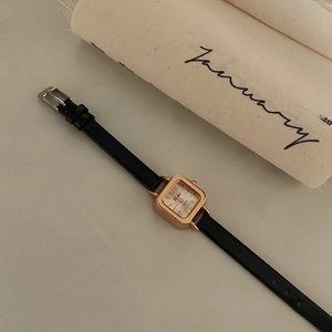 Close-up of minimalist square rose gold watch with white dial and slim black leather strap