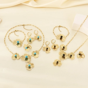 Detailed set of gold floral jewelry with turquoise and black center gems on beige fabric