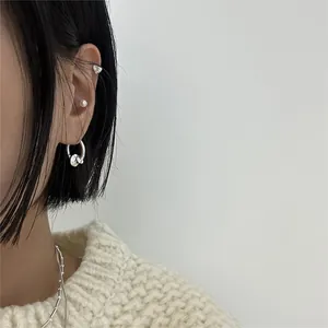 Close-up of minimalist silver earring set featuring heart stud, pearl, and hoop on model