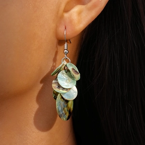 Detailed close-up of multilayered shell earrings with iridescent green and blue textures