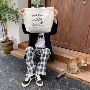 Close-up of a white canvas tote bag with black print held by a model on wooden steps