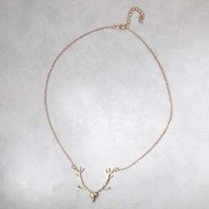Detailed view of a golden reindeer antler pendant necklace on a clean light grey background