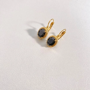 Detail of vintage gold earrings with oval black stones on textured white background