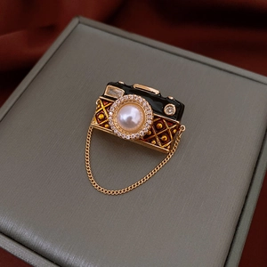 Macro detail of camera brooch with pearl inlay, golden chain, and crystal accents on a box