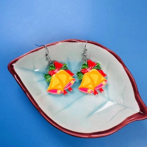 Christmas bell earrings with red bow and green leaves on a white ceramic plate