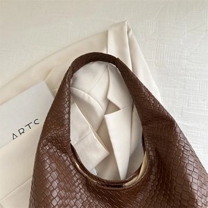 Chic brown woven leather hobo bag for women displayed on a white jacket and book