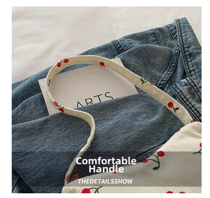 Detail of white corduroy shoulder bag featuring red cherry prints and soft handle