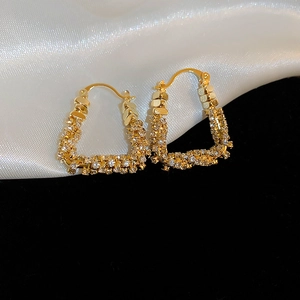 Macro shot of U-shaped gold plated earrings featuring micro-paved zircons on silk fabric