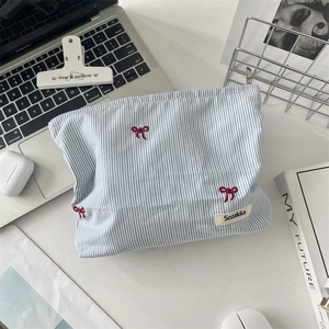Trousse de maquillage rayée bleue avec nœuds rouges sur bureau avec ordinateur