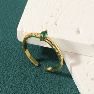 Minimalist gold open ring with green gemstone and textured band on white stone