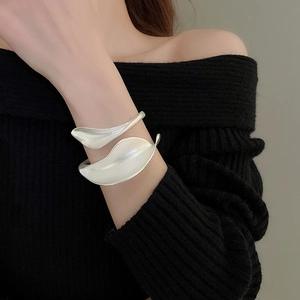 Detail of silver leaf-shaped open cuff bracelet with a matte metallic texture on wrist