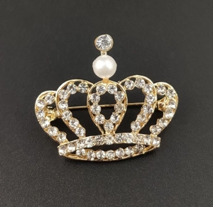 Macro view of crown brooch featuring white rhinestones and a central imitation pearl