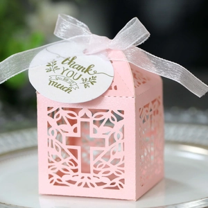 Close-up van roze lasergesneden geschenkdoos met kruispatroon, wit lint en bedankkaartje