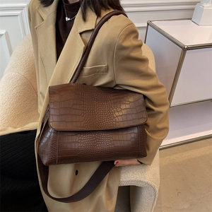 Brown crocodile pattern shoulder bag with flap design and fabric strap worn by a model