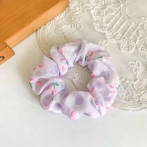 Close-up of purple scrunchie with pink cherry and heart patterns on soft fabric texture