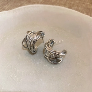 Macro shot of silver multi-layer spiral stud earrings on a beige ceramic plate