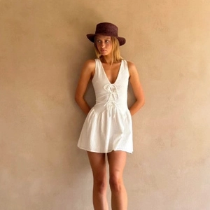 White sleeveless V-neck mini dress with ruffled hem and decorative tie-front design