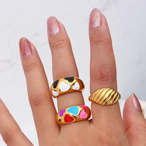 Close-up of gold 18k plated heart enamel rings and textured dome ring on marble surface