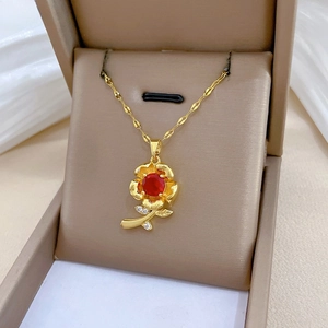Detail of a gold rose necklace with a red gem pendant in a beige jewelry gift box