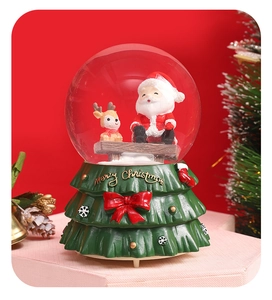 Macro view of Christmas snow globe with Santa and reindeer on a green tiered tree base