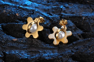 Detail macro shot of golden flower earrings with white pearls on a dark blue background