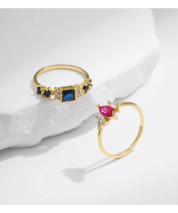 Detailed shot of gold-plated rings with blue square and pink marquise crystals on stone