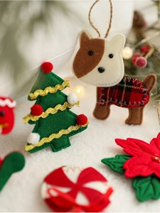 Detail of felt Christmas ornaments featuring a green tree and puppy on soft white fabric